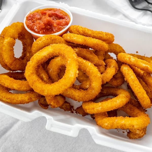 A white takeout container filled with golden-brown fried onion rings and a side of red marinara sauce.