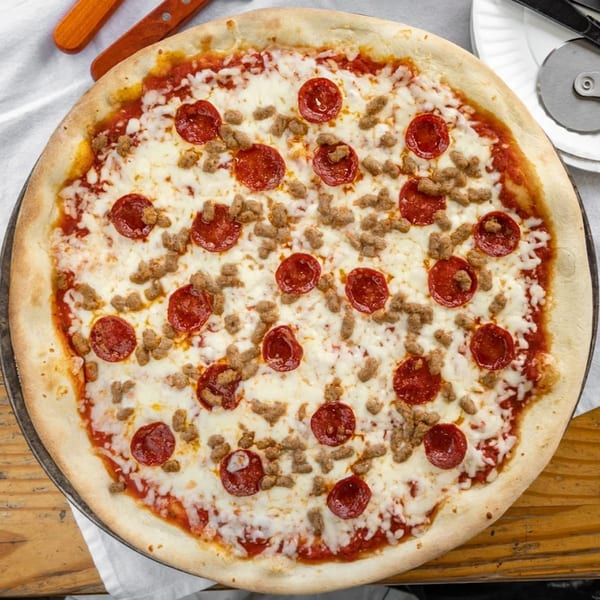 A Robola Pizzeria pizza with pepperoni and sausage, on a white tablecloth with a pizza cutter.
