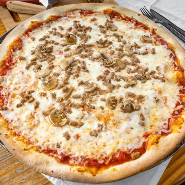 A Robola Pizzeria pizza with sausage and mushrooms, on a table with cutlery.