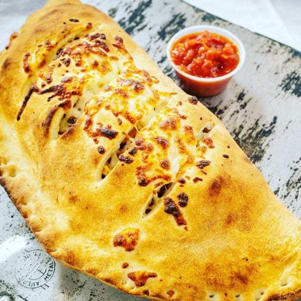 A golden-brown calzone with melted cheese on top, served with a side of red marinara sauce.