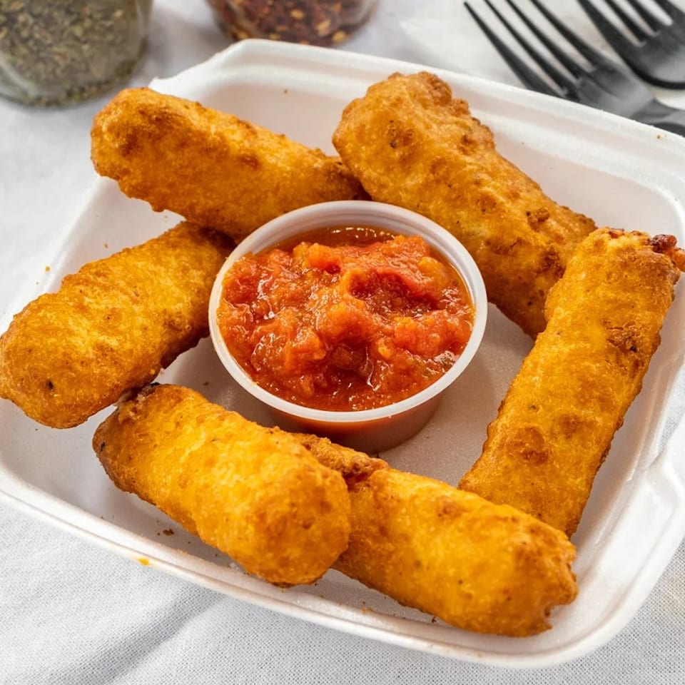 Golden-brown mozzarella sticks and a cup of red marinara sauce in a white takeout container.