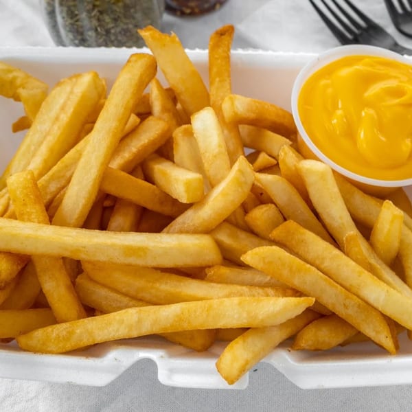 Golden french fries in a white container with a side of bright yellow cheese sauce.