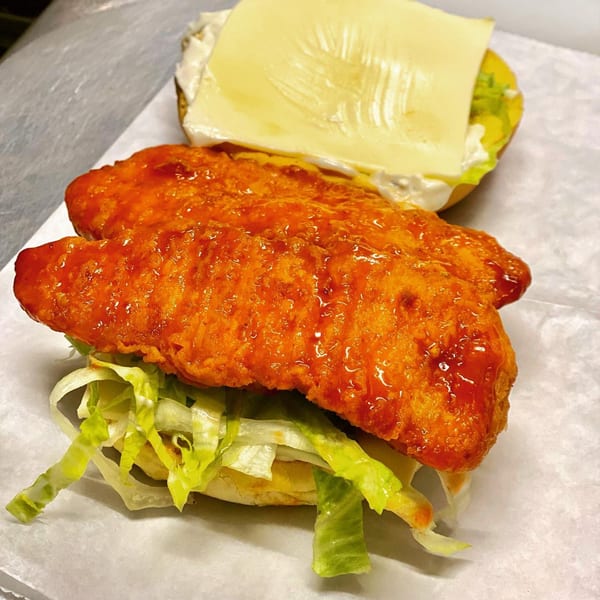 Open chicken sandwich with two crispy, sauced chicken fillets, lettuce, and a cheese slice on a bun.